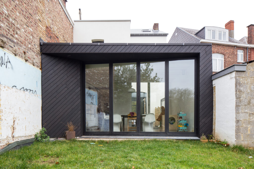 Extension contemporaine noire adossée au mur mitoyen en brique, rénovation à Gembloux