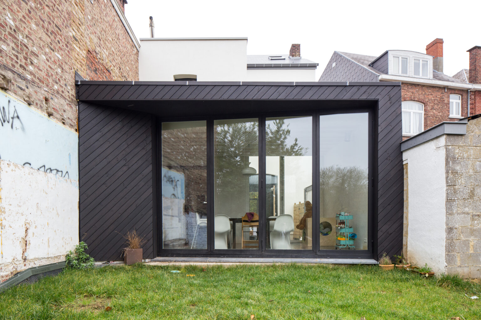 Extension contemporaine noire adossée au mur mitoyen en brique, rénovation à Gembloux