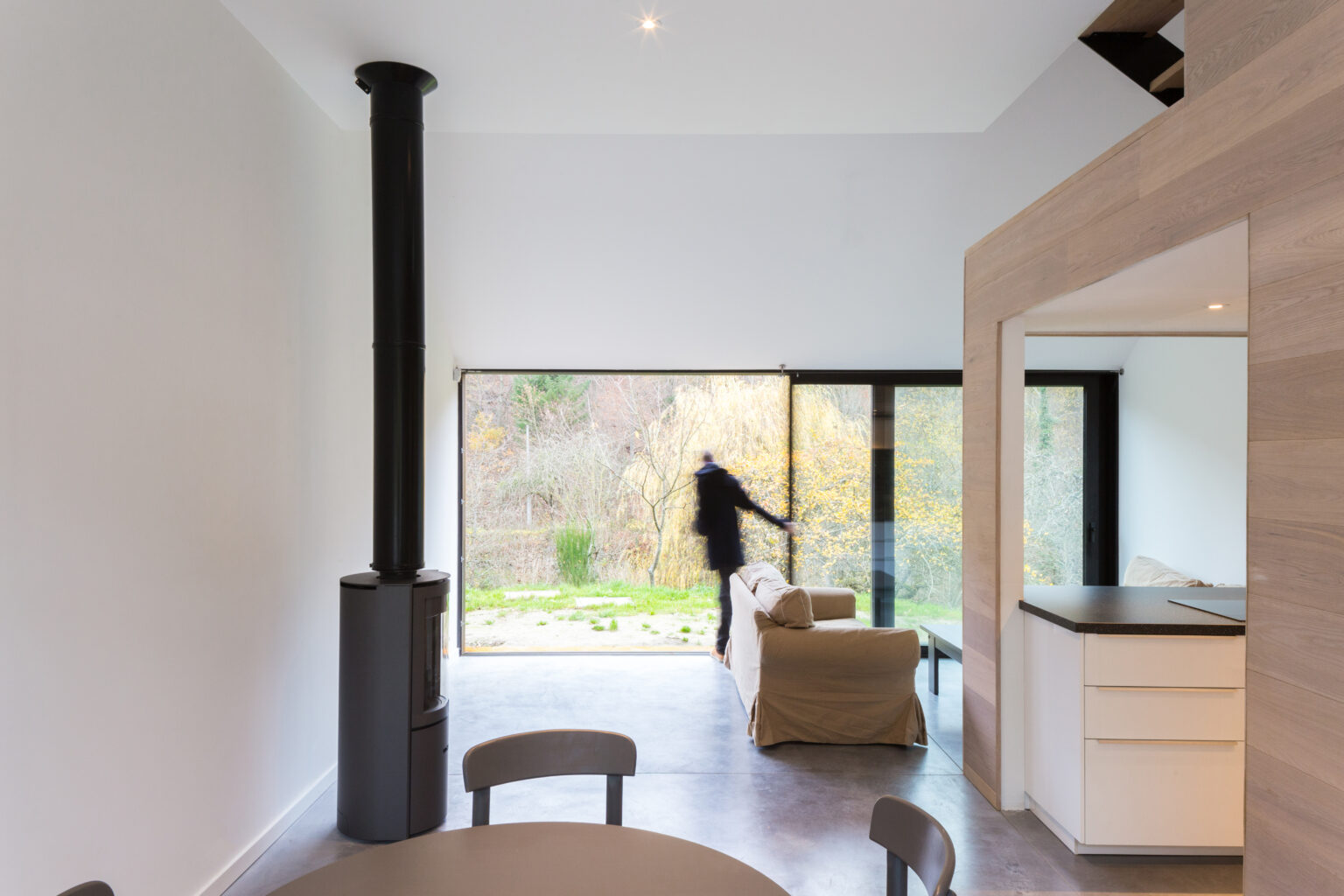 Salle à manger ouverte sur le paysage vallonné de Lustin, poêle à bois et menuiseries en bois clair