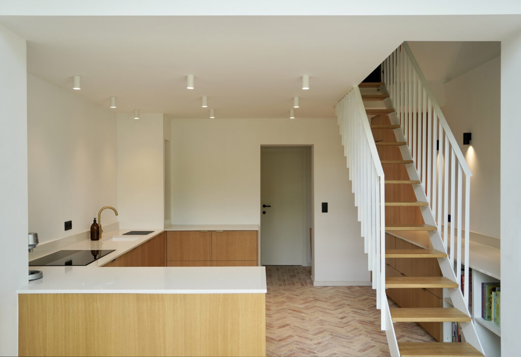 Cuisine en chêne et escalier blanc sur parquet à chevrons, maison rénovée à Auderghem