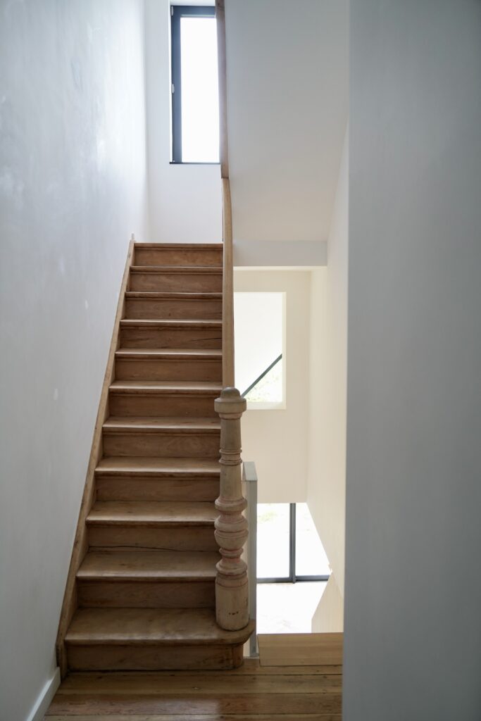 Escalier en bois et mur blanc éclairés par une fenêtre haute, maison à Auderghem