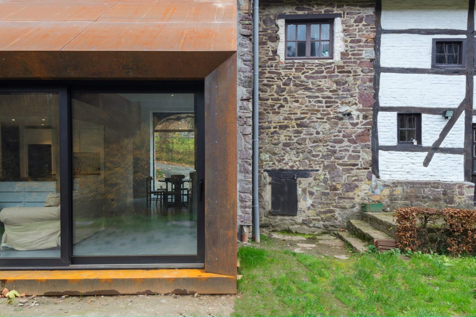 Extension en acier corten et baie vitrée adossée au mur en moellons de la grange de Lustin