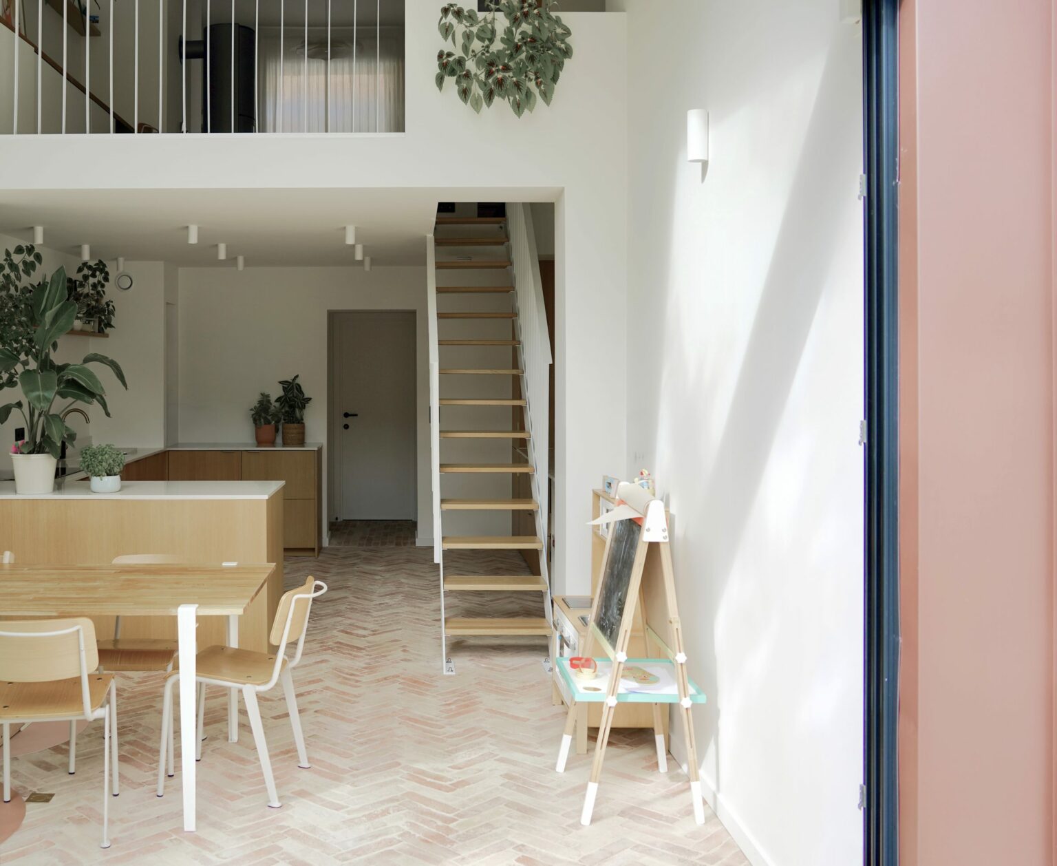 Table de salle à manger et escalier en acier blanc sur sol en briques à chevrons, rue de la Vignette